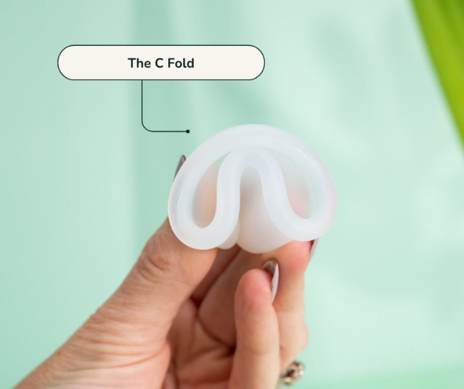 Hand holding a folded menstrual cup demonstrating the C-fold insertion technique.