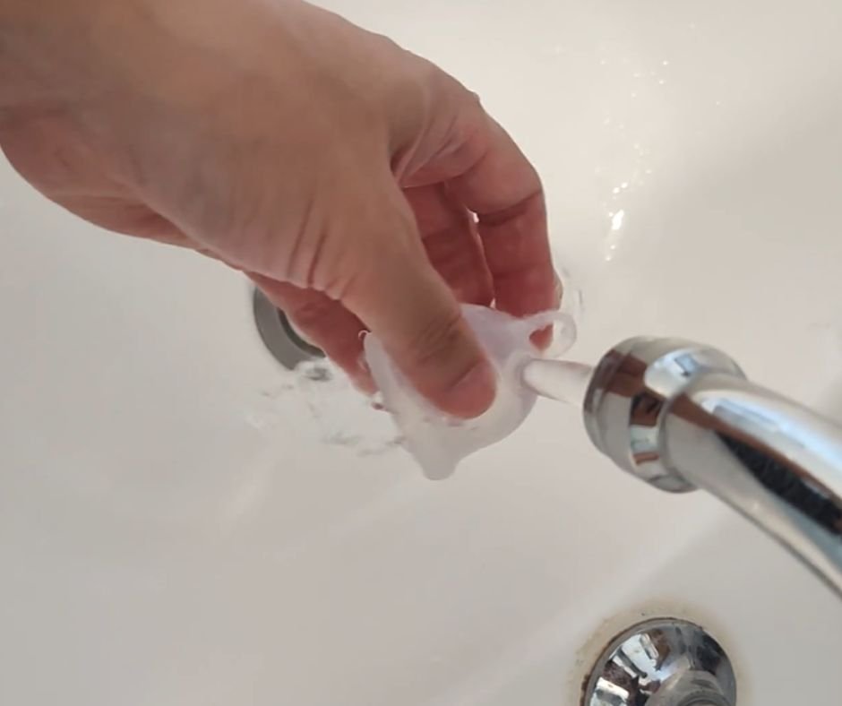 A silicone menstrual cup being rinsed with running tap water