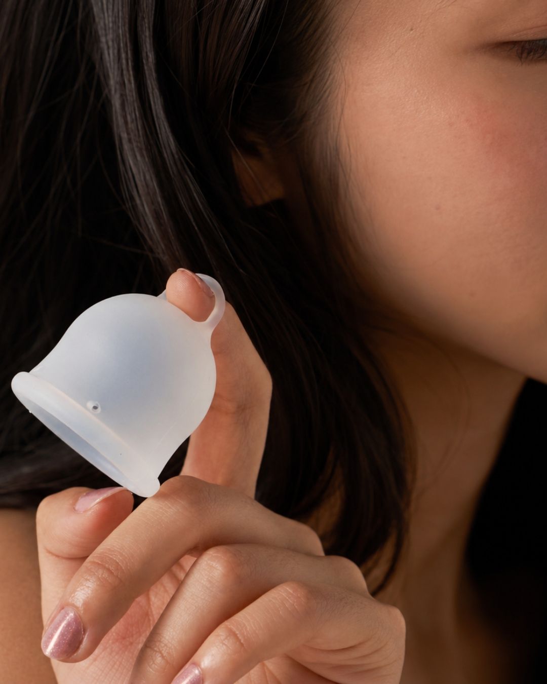 Person holding a silicone menstrual cup close to their face
